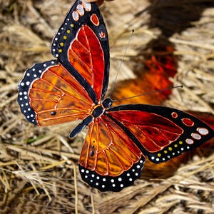 May include: A colorful butterfly with orange, red, and black wings. The butterfly has white polka dots along the edges of its wings. The wings are detailed with a stained glass effect. The butterfly is a decorative item.