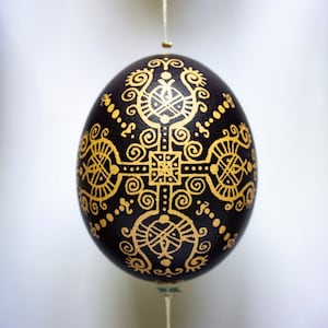 Peut inclure: Ornement en forme d'œuf noir avec des motifs dorés complexes et symétriques. L'ornement est suspendu par un fil fin, mettant en valeur un motif orné et détaillé. Le design présente des formes géométriques et des lignes tourbillonnantes, pour Pâques ou les fêtes.