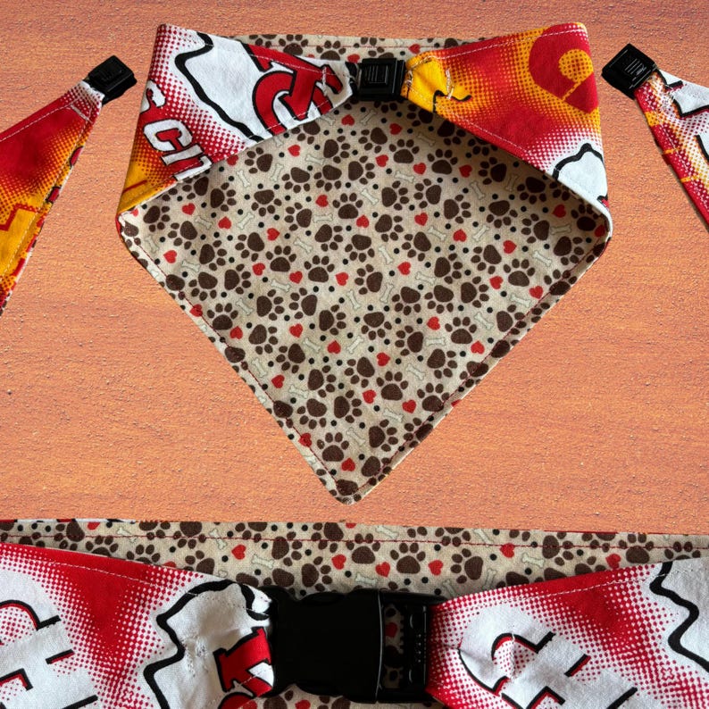 May include: Dog bandana with a reversible design. One side features a pattern of brown paw prints and red hearts on a tan background. The other side has a red, white, and yellow design with a black buckle closure. The bandana is made of fabric.