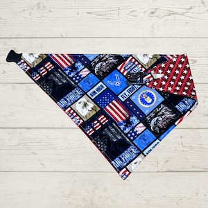 May include: A patriotic dog bandana featuring a patchwork design with Air Force emblems, American flags, and the text "AIR FORCE", "AIM HIGH", and "FLY, FIGHT". The bandana has a red and white star pattern on one corner and a black adjustable buckle.
