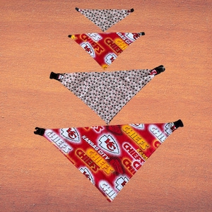 May include: Four triangular pet bandanas. Two are red with "Chiefs" and "Kansas City" text and logos. The other two are white with a repeating pattern of red paw prints and black accents. Each bandana has a black buckle.
