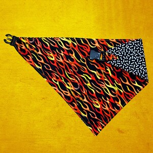 May include: A triangular dog bandana with a flame pattern in red, yellow, and orange on a black background. The reverse side features a black and white bone pattern. It has a black plastic buckle and adjustable strap.