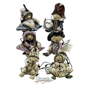 May include: Six ceramic figurines with colorful clothing and hats. Each figurine has a smiling face and is holding a small bell. The figurines are hanging from strings and are made in Italy.