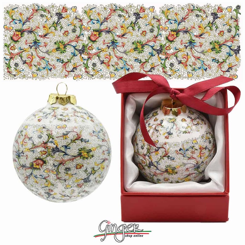 May include: A white ceramic Christmas ornament with a gold top and a colorful floral pattern. The ornament is in a red box with a red ribbon.