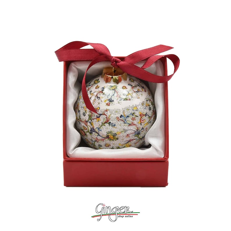 May include: A white ceramic Christmas ornament with a colorful floral design, in a red box with a red ribbon.