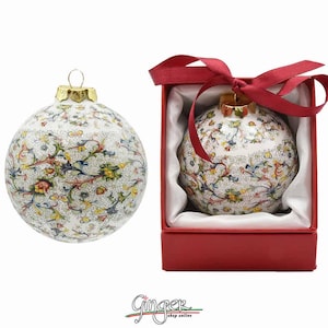 May include: A white ceramic Christmas ornament with a colorful floral pattern. The ornament is in a red box with a white satin lining and a red ribbon.