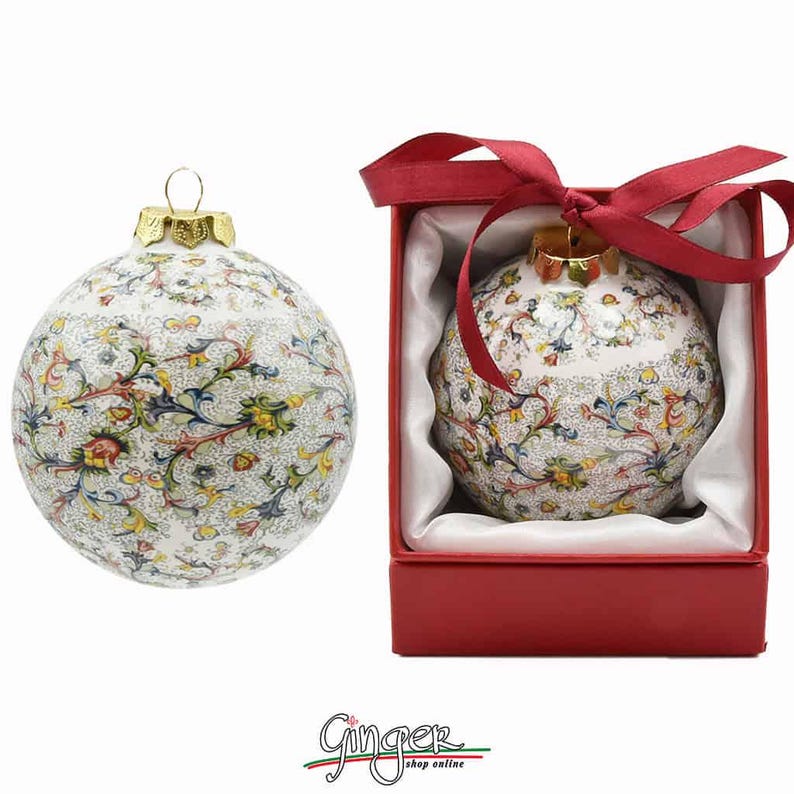 May include: A white ceramic Christmas ornament with a colorful floral pattern. The ornament is in a red box with a white satin lining and a red ribbon.