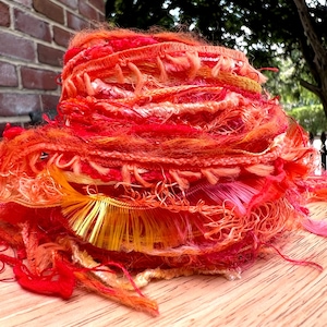 May include: A pile of colorful yarn in shades of red, orange, and yellow. The yarn is made of a variety of fibers, including cotton, silk, and wool. The yarn is perfect for knitting, crocheting, or weaving.