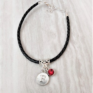 May include: Black leather bracelet with a silver charm featuring the letter "F" and a red rhinestone.