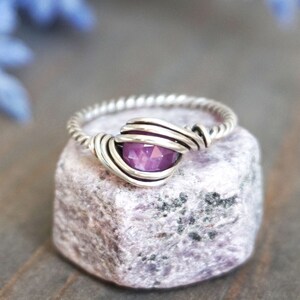 May include: A silver ring with a twisted band and a purple gemstone set in the centre.