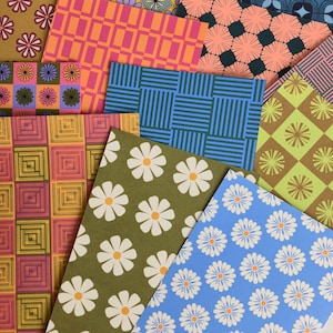 May include: A collection of rectangular sheets featuring various patterns including retro-style daisies in white and yellow, geometric grids in orange and pink, striped blue blocks, and diamond shapes in green and brown, layered in a scattered arrangement.