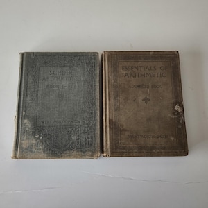 May include: Two antique arithmetic textbooks. The book on the left is gray and reads "School Arithmetic Book Two". The book on the right is tan and reads "Essentials of Arithmetic Advanced Book". Both books are worn.