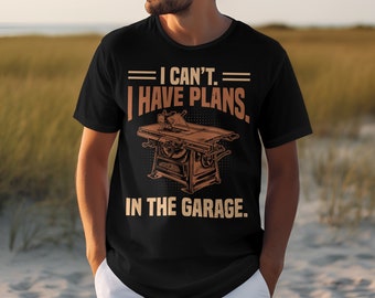 Op de afbeelding: Zwart t-shirt met de tekst "I can't. I have plans. In the garage." in een bruin, vintage lettertype. Het shirt heeft een afbeelding van een tafelzaag. Het shirt is gemaakt van een zacht materiaal.