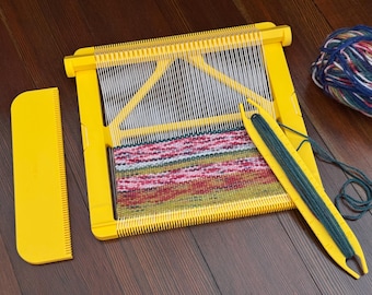 Peut inclure: Un métier à tisser jaune avec des fils de chaîne blancs et un textile partiellement tissé en rouge, vert et rose. Un peigne jaune et une navette avec du fil vert sont également présents, ainsi qu'une pelote de fil multicolore.