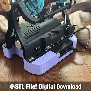 Pode incluir: Uma bobinadeira de fio preta e roxa com uma roda azul e detalhes em madeira. A máquina está conectada a uma fonte de alimentação e está sobre uma superfície de madeira. O texto "STL File! Digital Download" está na parte inferior da imagem.