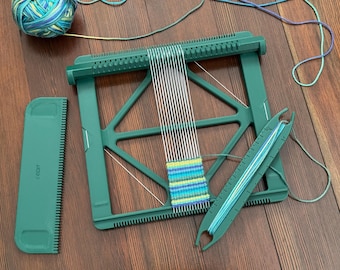 Peut inclure: Un métier à tisser vert avec des fils blancs et une pièce partiellement tissée en bleu et vert. Un peigne vert et une navette avec du fil bleu sont également présents. Une pelote de fil bleu et vert est à proximité.