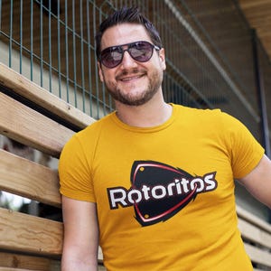 Pode incluir: Um homem vestindo uma camiseta amarela com um logotipo preto e vermelho que diz "Rotoritos".