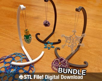 May include: Three 3D printed stands with different colored crocheted ornaments hanging from them. The stands are black, white, and gray. The ornaments are a purple flower, a white snowflake, and a green lightbulb. The text "Bundle STL File! Digital Download" is at the bottom of the image.