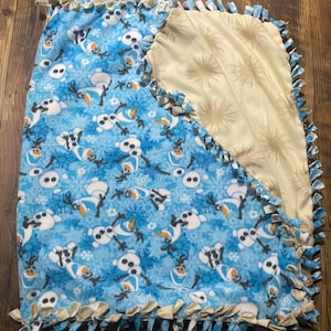 May include: A blue and white fleece tie blanket with a pattern of Olaf from Frozen. The blanket has a tan fleece backing.