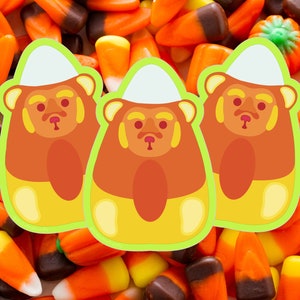 May include: Three candy bear stickers with a candy corn design, set against a background of candy corn. The bears are orange, yellow, and white, with a green outline. A festive and fun Halloween theme.