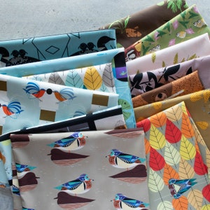 May include: A stack of colorful fabric panels with various bird and nature-inspired designs. The fabrics feature a variety of patterns, including geometric shapes, floral motifs, and abstract designs. The fabrics are arranged in a staggered pattern, creating a visually appealing display.