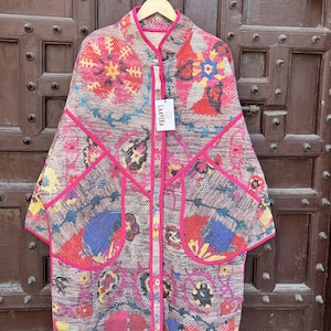 May include: A long-sleeved jacket featuring a vibrant, multi-colored floral and paisley pattern in shades of red, blue, yellow, and pink. The garment has a bright pink trim along the edges, a mandarin collar, and two large front pockets. A white tag reads LAAVEKA.