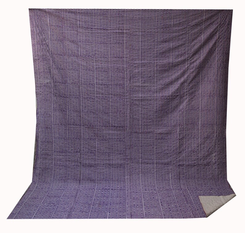May include: A purple and white striped fabric with a repeating geometric pattern. The fabric is folded in half and the edges are visible.