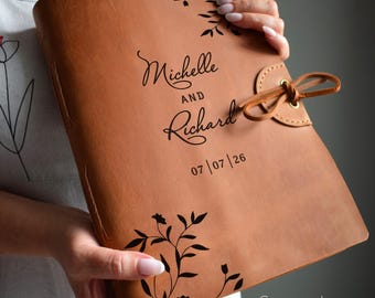 May include: A cognac-colored leather journal with the names "Michelle and Richard" and the date "07/07/26" printed in black. The journal features floral designs and a leather tie closure.