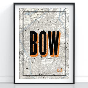 May include: A framed wall art print featuring a vintage black and white map of the Bow area in London. The word BOW is printed in large, bold black letters with an orange drop shadow, and the text E3 appears in orange in the bottom right corner.