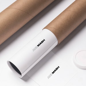 May include: A white poster tube with the text "ANDMASH" printed on it. The tube is partially unrolled and is sitting on a white surface. There is a brown cardboard tube behind it and a white round cap on the surface.