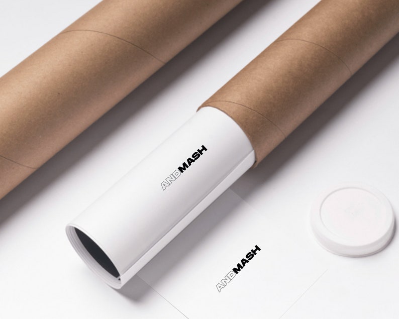May include: A white poster tube with the text "ANDMASH" printed on it. The tube is partially unrolled and is sitting on a white surface. There is a brown cardboard tube behind it and a white round cap on the surface.