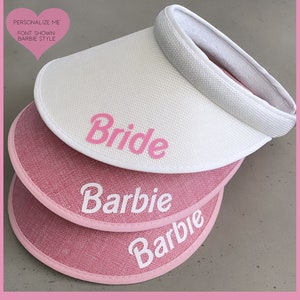 May include: Three pink and white sun visors with the words "Bride", "Barbie", and "Barbie" written on them. The visors are stacked on top of each other.