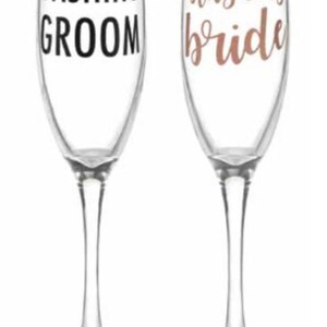 May include: Two champagne flutes with the words "Dashing Groom" and "Blushing Bride" in black and rose gold lettering.