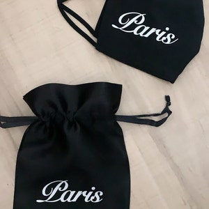 May include: Black fabric face mask and a black drawstring bag, both with the word "Paris" written in white cursive lettering.