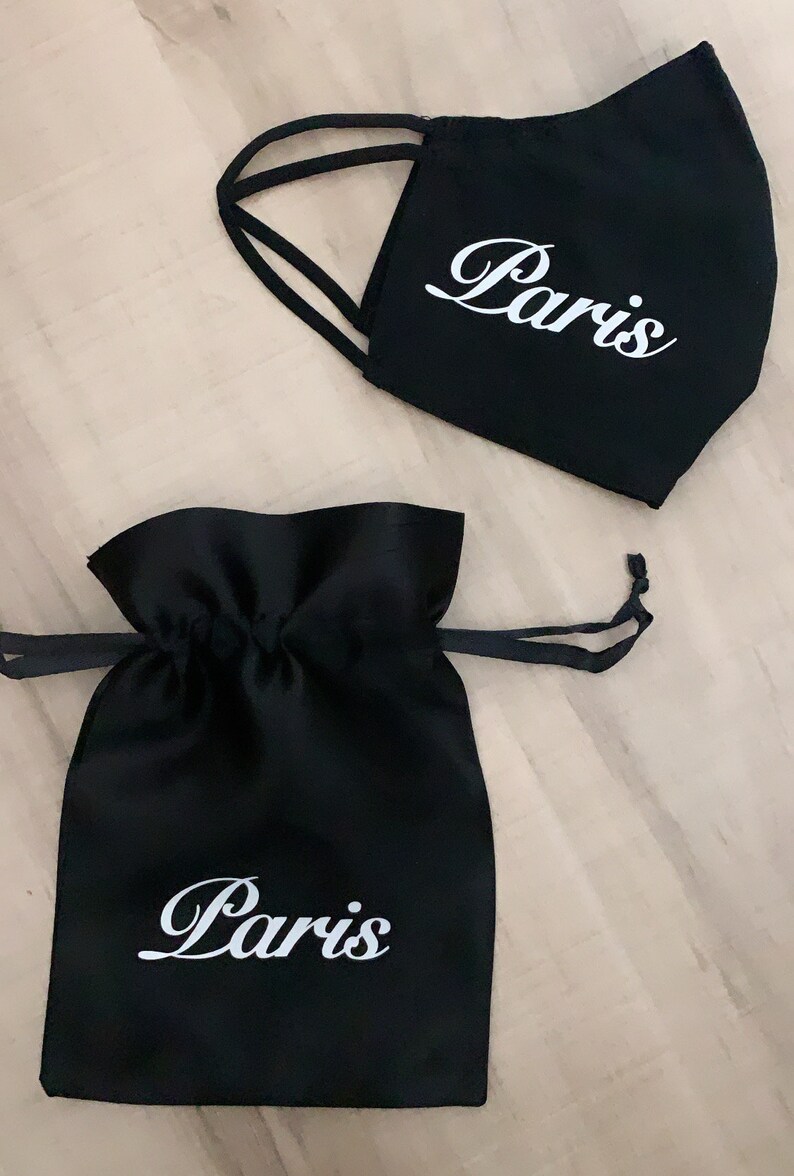 May include: Black fabric face mask and a black drawstring bag, both with the word "Paris" written in white cursive lettering.