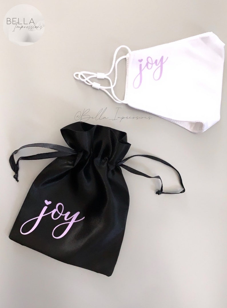 May include: A black satin drawstring bag with the word "joy" in purple lettering. A white face mask with the same lettering is also included.