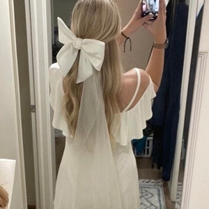 May include: A white off-the-shoulder dress with a large white bow in the hair.