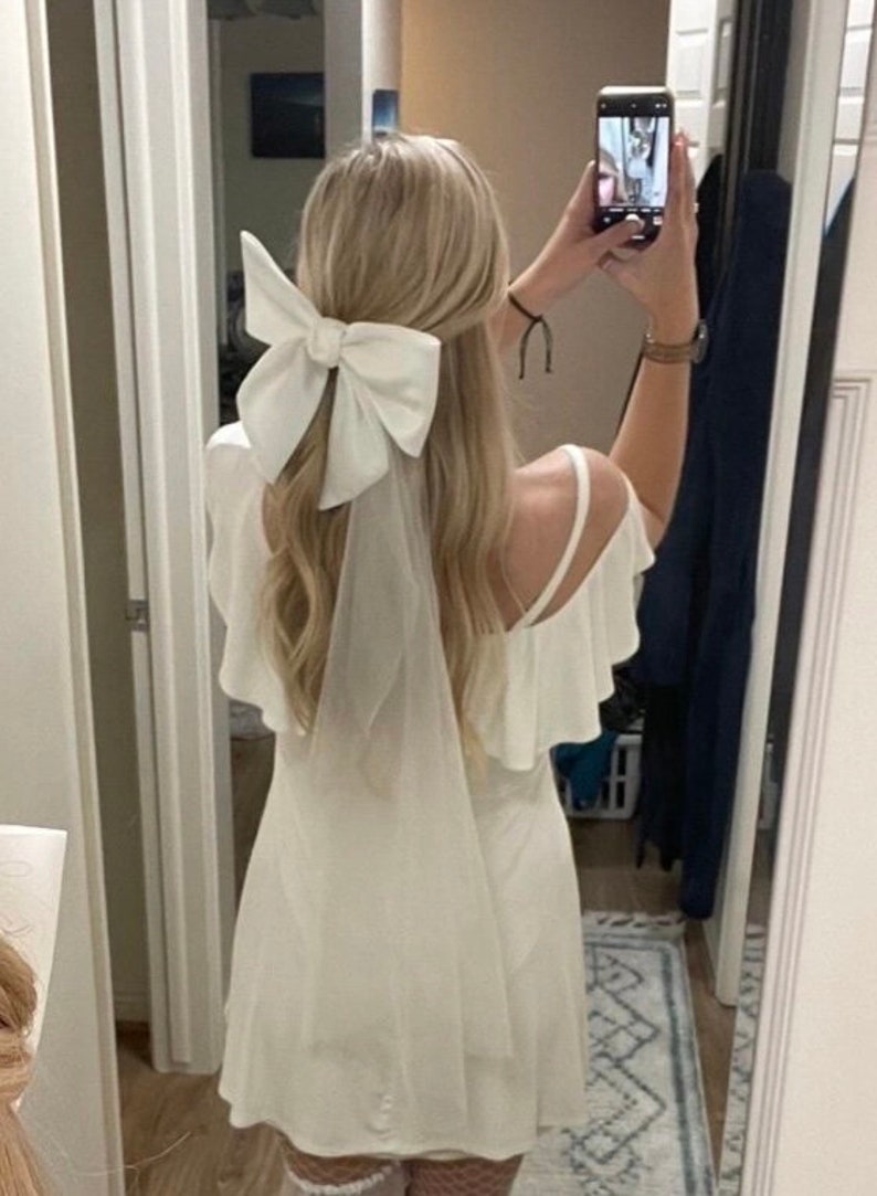 May include: A white off-the-shoulder dress with a large white bow in the hair.