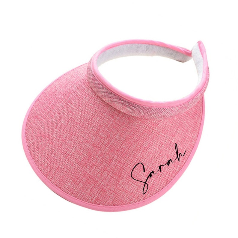 Op de afbeelding: Roze zonneklep met een zwarte geborduurde naam "Sarah" aan de voorkant.