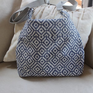 May include: A blue and white geometric patterned tote bag with a gray shoulder strap.
