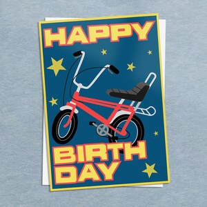 Könnte beinhalten: Eine Geburtstagskarte mit einer roten Fahrradillustration auf dunkelblauem Hintergrund. Die Worte "HAPPY BIRTH DAY" sind in gelben Blockbuchstaben gehalten. Gelbe Sterne sind um das Fahrrad herum verstreut.