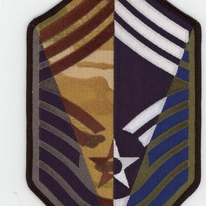 Puede incluir: Un parche de rango militar marrón, beige y azul con una estrella blanca y tres rayas blancas. El parche está bordado con un patrón de camuflaje.