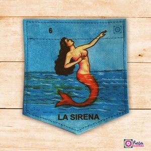 May include: A blue denim pocket with a colorful illustration of a mermaid with red hair and a red tail. The mermaid is swimming in blue water. The text "LA SIRENA" is printed below the mermaid.