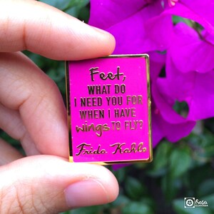 May include: A pink enamel pin with gold lettering that reads "Feet, What do I need you for when I have wings to fly?" and "Frida Kahlo".