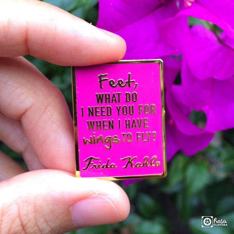 May include: A pink enamel pin with gold lettering that reads "Feet, What do I need you for when I have wings to fly?" and "Frida Kahlo".