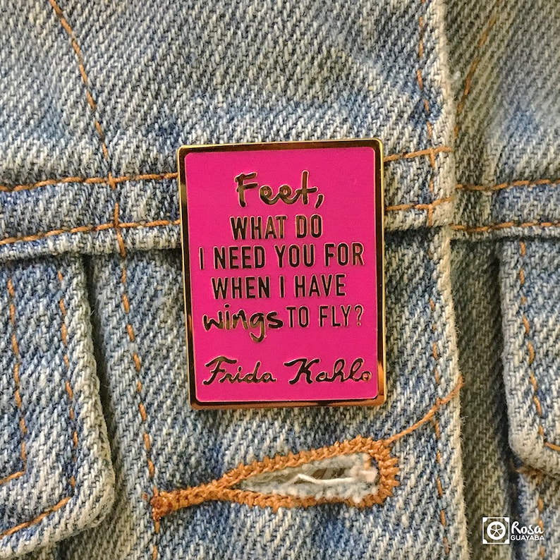 May include: Pink enamel pin with gold trim featuring a quote by Frida Kahlo: "Feet, what do I need you for when I have wings to fly?"