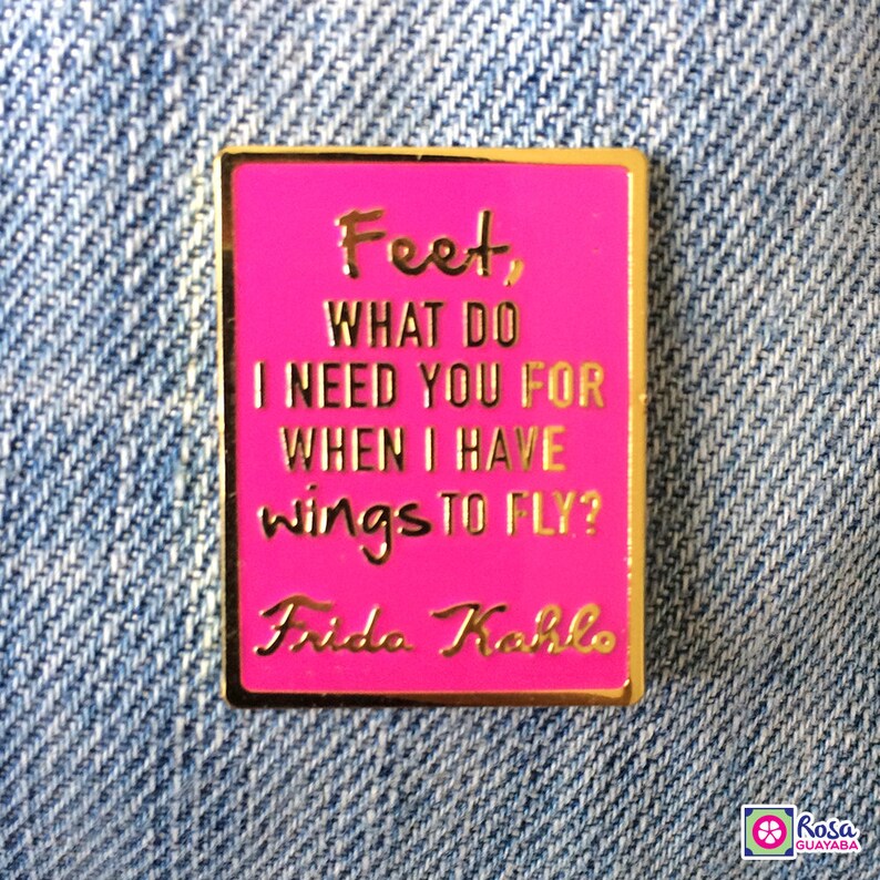 May include: Pink enamel pin with gold lettering featuring a quote by Frida Kahlo: "Feet, what do I need you for when I have wings to fly?"