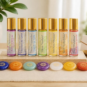 May include: Seven glass roller bottles with gold caps, each labelled with a chakra name and affirmation, arranged in a row. Below them are seven smooth, colourful stones, each engraved with a unique chakra symbol, resting on a rectangular stone base.