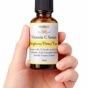 May include: A brown glass bottle of Vitamin C Serum held in a hand. The label reads "PEARL'S Natural Cosmetic" and "Brighten/Firm/Tone". The bottle contains 35ml of serum and lists ingredients like Hyaluronic Acid and Centella Asiatica Extract.