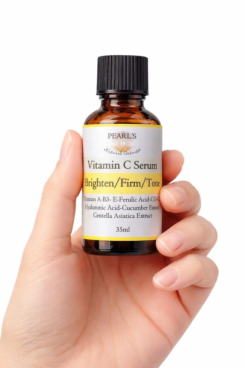 May include: A brown glass bottle of Vitamin C Serum held in a hand. The label reads "PEARL'S Natural Cosmetic" and "Brighten/Firm/Tone". The bottle contains 35ml of serum and lists ingredients like Hyaluronic Acid and Centella Asiatica Extract.